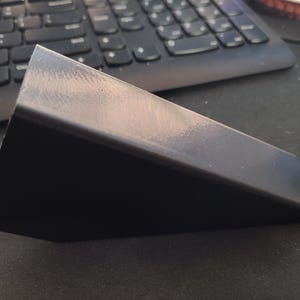 May include: A black plastic wedge-shaped object. The object is smooth and has a slight sheen.
