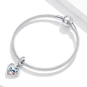 May include: A silver charm bracelet with a heart-shaped charm featuring a colourful cityscape. The bracelet has a clasp that reads "Love Forever".