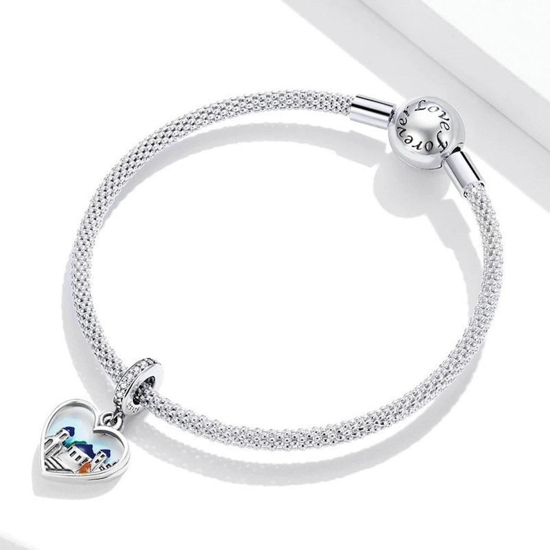 May include: A silver charm bracelet with a heart-shaped charm featuring a colourful cityscape. The bracelet has a clasp that reads "Love Forever".