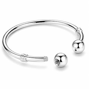 May include: A silver-toned open bangle bracelet featuring a smooth, polished finish. The bracelet has two spherical ends, one of which is detachable, revealing a threaded screw mechanism on the end of the bangle band for secure closure.