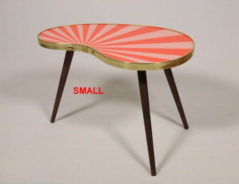 May include: A kidney-shaped side table with three dark brown tapered wooden legs and a gold-toned metal rim. The tabletop features a sunburst pattern in alternating shades of coral and light pink. The word SMALL is printed in red.