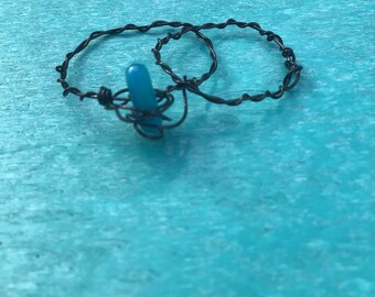 May include: Two black wire rings with a turquoise blue glass bead in the centre.