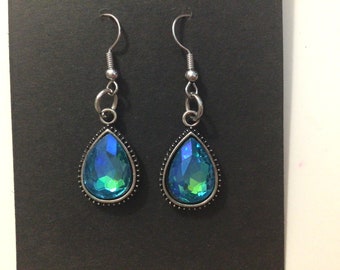 May include: A pair of teardrop earrings featuring iridescent blue and green stones. The stones are set in a silver-coloured metal frame with a beaded edge. The earrings have a silver-coloured hook closure.
