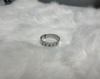 May include: A silver ring with the word "PEACE" engraved on it.