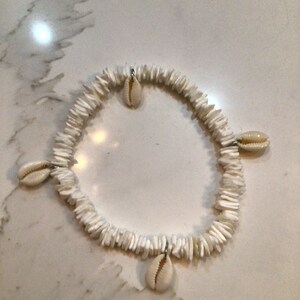 Puede incluir: Pulsera de conchas blancas con cuatro conchas de cauri blancas colgando de ella.