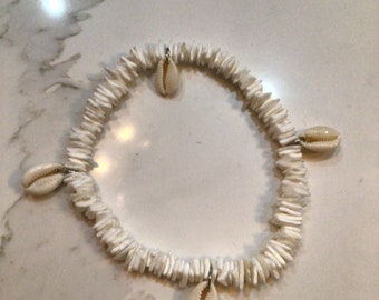 May include: White shell bracelet with four white cowrie shells hanging from it.