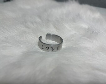 May include: A silver adjustable ring with the word "LOVE" engraved on it.