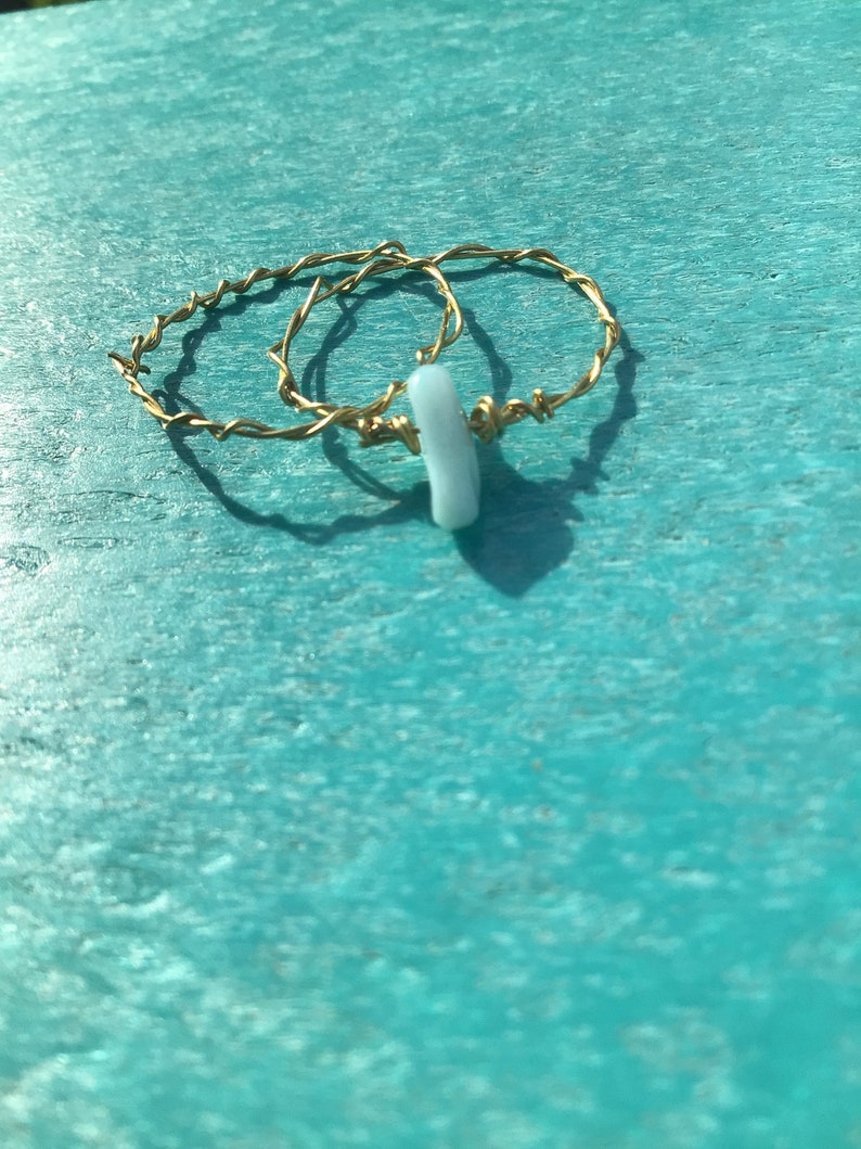 Puede incluir: Dos anillos de alambre dorado envueltos con un dije de piedra azul claro.