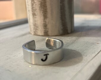 May include: A silver adjustable ring with the letter "J" engraved on the band.