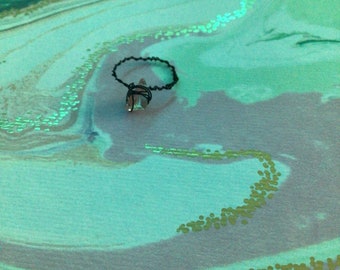 May include: A black wire ring with a clear crystal charm on a green and blue marbled background.