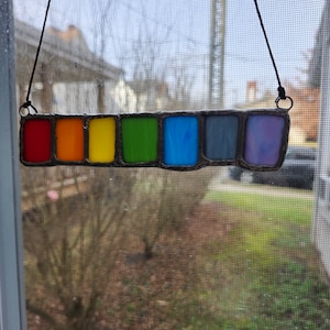 May include: A stained glass rainbow hanging in a window. The rainbow is made of seven colors: red, orange, yellow, green, blue, indigo, and violet.