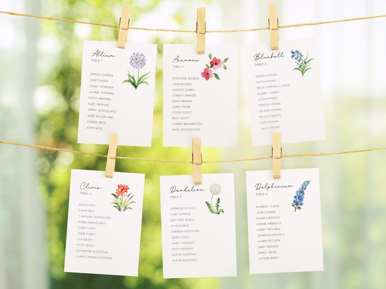 Puede incluir: Seis tarjetas blancas con ilustraciones florales y nombres de mesas e invitados. Las tarjetas est&aacute;n colgadas de una cuerda con pinzas de madera. Las flores est&aacute;n pintadas en estilo acuarela. Los nombres de las mesas son: Allina, Anemone, Bluebell, Clivia, Dandelion y Delphinium.