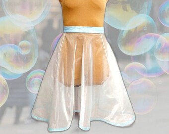 May include: A mannequin wearing a transparent skirt with a light blue trim and a matching light blue waistband. The mannequin is tan and has a turtleneck. The skirt is knee-length and has a slight A-line shape.