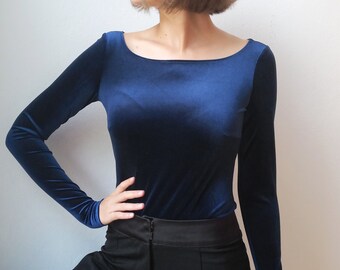 May include: A woman wearing a navy blue velvet long-sleeve top with a scoop neck and black pants.