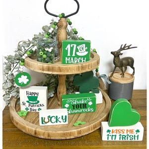 May include: A two-tier wooden tiered tray decorated with green and white beads, shamrock-themed wooden signs, and a green heart with the text "Kiss Me I'm Irish".