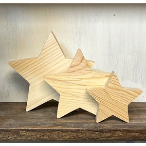 May include: Three wooden stars of varying sizes, all made of natural light brown wood. The stars are arranged in a row, with the largest star on the left and the smallest star on the right.