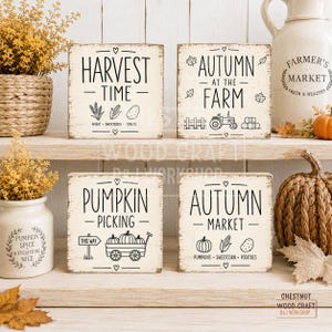 May include: Four square wooden signs with distressed white paint and black text. The signs feature seasonal graphics including wheat, corn, potatoes, a tractor, a fence, hay bales, a pumpkin wagon, and text reading Harvest Time, Autumn at the Farm, Pumpkin Picking, and Autumn Market.