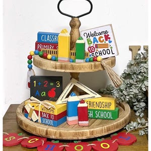 May include: A two-tiered wooden serving tray with a black handle, decorated with back to school themed wooden blocks, pencils, and a welcome back to school sign. The tray is surrounded by a red apple garland with the word "SCHOOL" spelled out.