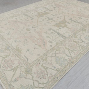 May include: A cream-colored rug with a delicate floral pattern in shades of pink and green. The rug has a fringed edge and a subtle distressed look.