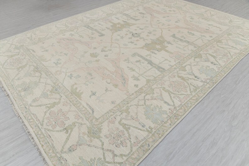 May include: A cream-colored rug with a delicate floral pattern in shades of pink and green. The rug has a fringed edge and a subtle distressed look.