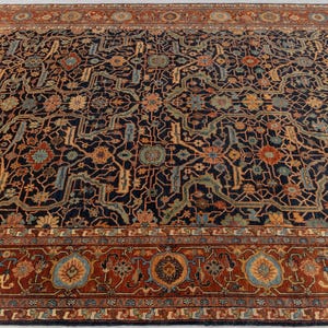 May include: A large, rectangular area rug with an intricate floral pattern. The rug features a dark navy blue background with a detailed design in shades of rust, gold, and teal. A wide border in rust color frames the central design.