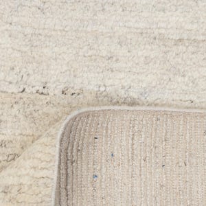 May include: A close-up of a white rug with a textured surface. The rug has a fringe border and is made of natural fibers.