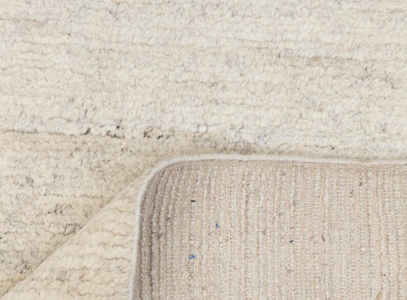 May include: A close-up of a white rug with a textured surface. The rug has a fringe border and is made of natural fibers.