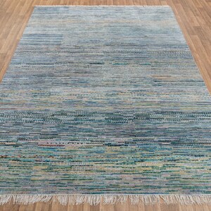 May include: A rectangular area rug with a textured, horizontal striped pattern in shades of blue, green, and beige. The rug has a fringe on the shorter ends and is placed on a wooden floor.