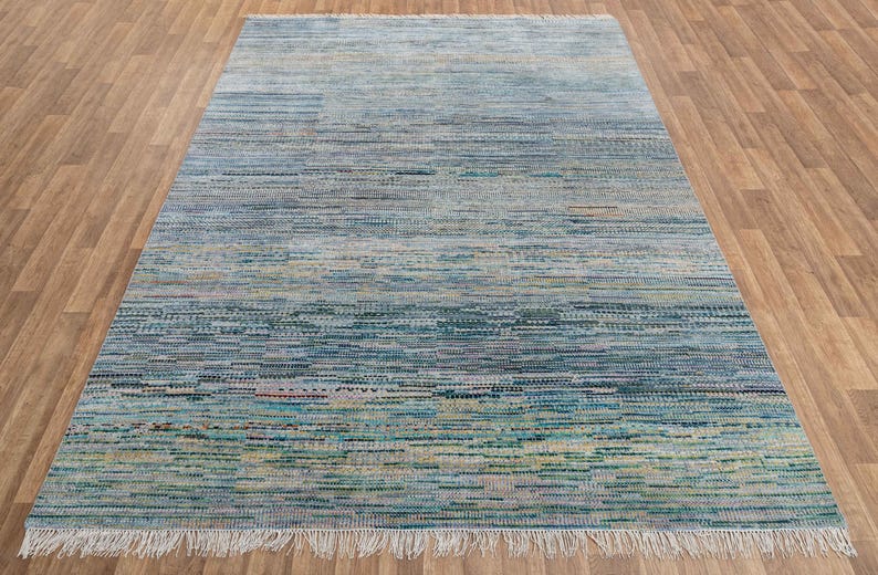 May include: A rectangular area rug with a textured, horizontal striped pattern in shades of blue, green, and beige. The rug has a fringe on the shorter ends and is placed on a wooden floor.