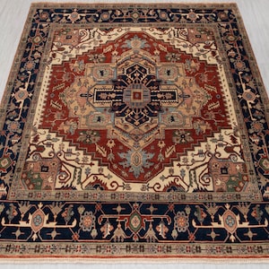 Pode incluir: Um tapete retangular com um design intrincado e simétrico. O tapete apresenta um medalhão central em tons de vermelho, azul marinho, bege e toques de verde e azul claro. A borda é azul marinho escuro com padrões florais.