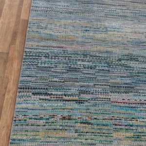 May include: A rectangular area rug with a textured, woven design. The rug features a blend of blue, green, yellow, and red hues, creating a multi-colored striped pattern. The rug has a fringed edge.
