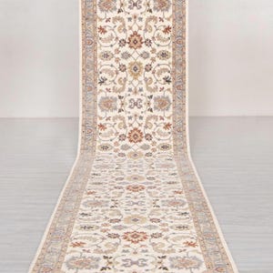 Puede incluir: Alfombra de pasillo de color marfil con un intrincado diseño floral en tonos marrón, azul y dorado. La alfombra presenta un borde detallado y flecos en los extremos, adecuada para pasillos o entradas.