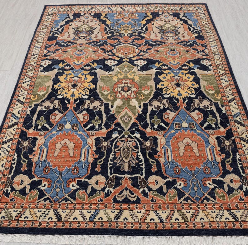 May include: A rectangular rug with a detailed, symmetrical design. The rug has a dark navy blue base with a complex pattern in shades of orange, blue, green, and beige. The border features a repeating geometric pattern.