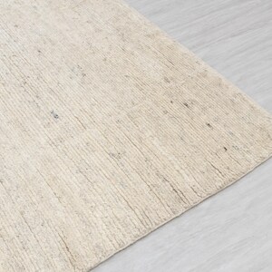 May include: A close-up of a cream-colored rug with a textured, woven surface. The rug has a subtle, natural pattern and a slightly rough texture.