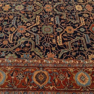 May include: A detailed, close-up view of a patterned rug. The rug features a dark navy blue background with an intricate design in shades of rust, gold, and teal. The border has a repeating floral pattern in rust and blue. The rug's design is symmetrical.