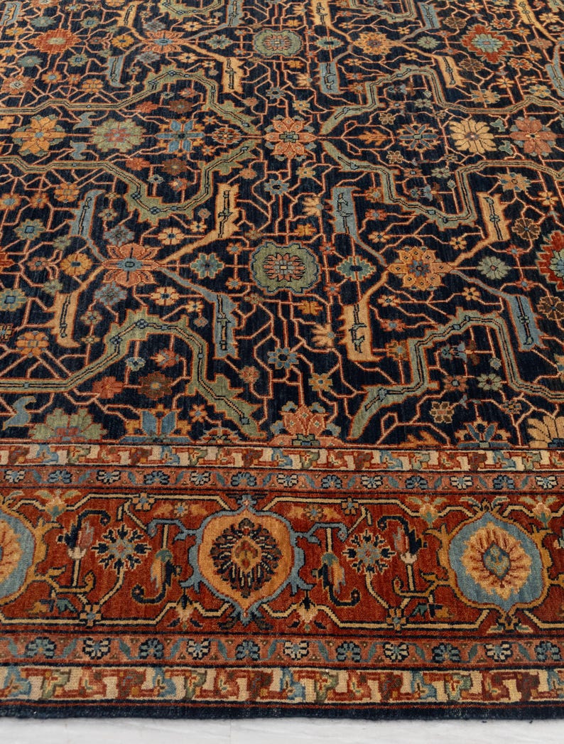 May include: A detailed, close-up view of a patterned rug. The rug features a dark navy blue background with an intricate design in shades of rust, gold, and teal. The border has a repeating floral pattern in rust and blue. The rug's design is symmetrical.