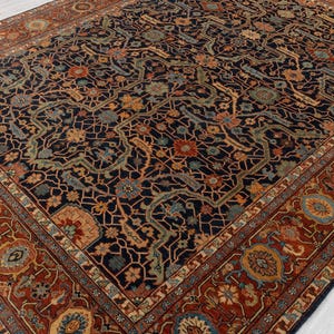 May include: An ornate, rectangular rug with a dark navy blue field and a detailed floral pattern in shades of orange, teal, and beige. The border is a rich reddish-brown with repeating floral medallions. The rug's design is intricate and traditional.