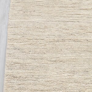 May include: A close-up of a cream-colored woven rug with a textured surface. The rug has a subtle, natural pattern.