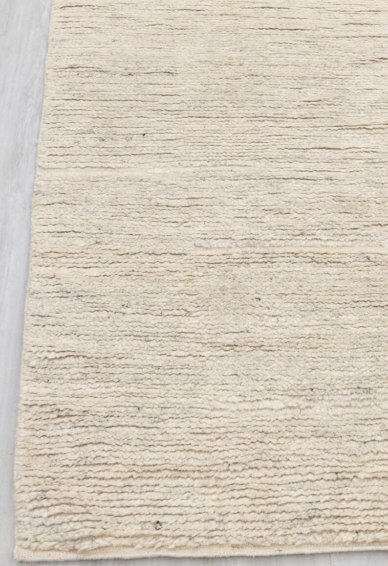 May include: A close-up of a cream-colored woven rug with a textured surface. The rug has a subtle, natural pattern.