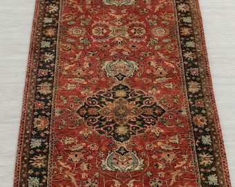 May include: A rectangular runner rug with an intricate, symmetrical pattern. The rug features a predominantly red field with black borders and accents of green, blue, and gold. The design includes floral and geometric motifs.