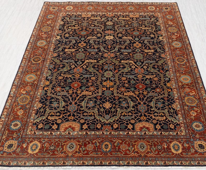 May include: A large, rectangular area rug with an intricate, traditional design. The rug features a dark navy blue central field with a complex pattern of floral and geometric motifs in shades of rust, green, and gold. A wide border in rust-red frames the design.