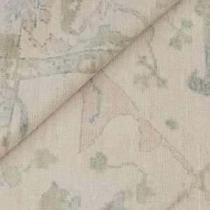 May include: Close-up of a light beige rug with a subtle floral pattern in shades of blue and pink.