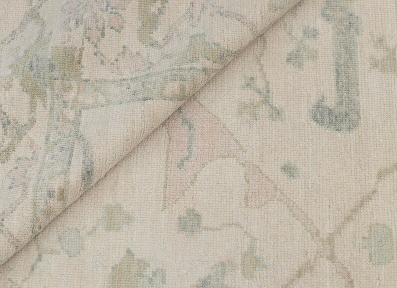 May include: Close-up of a light beige rug with a subtle floral pattern in shades of blue and pink.