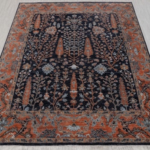Puede incluir: Una alfombra persa tradicional con un fondo azul oscuro y intrincados patrones florales en tonos de naranja, rojo y azul. La alfombra tiene un borde con un patrón repetitivo de hojas y flores estilizadas.