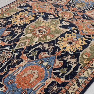 May include: A rectangular rug with a detailed, traditional design. The rug has a dark navy blue background with a repeating pattern of floral and geometric shapes in shades of orange, blue, green, and yellow. The border has a cream and brown geometric pattern.