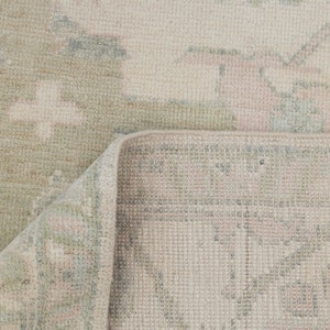 May include: A close-up of a light beige rug with a subtle pattern. The rug has a woven texture and a fringed edge.