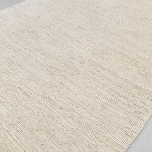 May include: A close-up of a light beige woven rug with a subtle texture. The rug has a natural, organic look and feel.