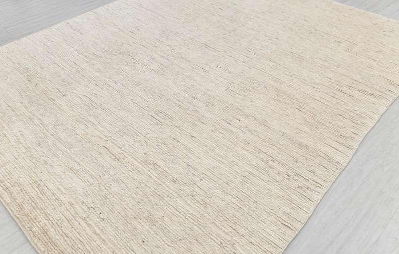 May include: A close-up of a light beige woven rug with a subtle texture. The rug has a natural, organic look and feel.