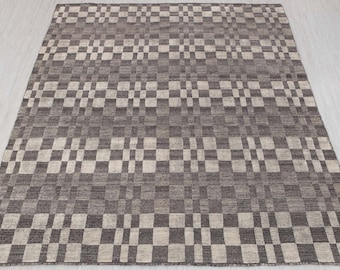 May include: A rectangular rug with a geometric pattern. The rug features a repeating design of alternating light and dark gray squares and rectangles. The rug is made of a woven material and has a textured appearance.