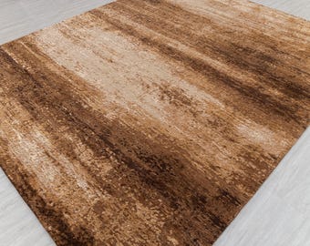 May include: A rectangular rug with a textured surface. The rug features a blend of brown and beige tones, with a pattern of long, irregular strokes. The color palette includes shades of light brown, medium brown, and dark brown.
